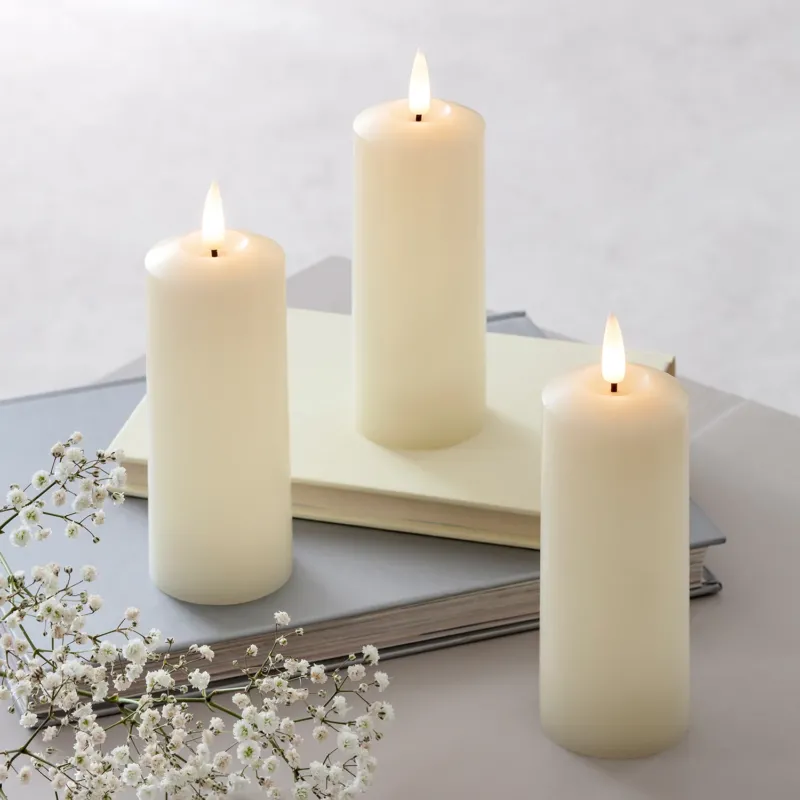 Drei LED-Kerzen stehen angeschaltet auf einem weißen Tisch.