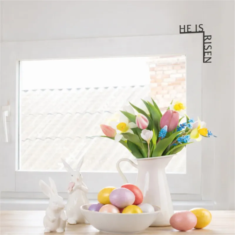 Decorative setup with Easter eggs, flowers, and 'He Is Risen' sign on a white background