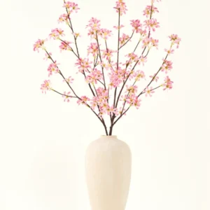Eine hohe beige Keramikvase enthält mehrere Zweige des künstlichen Blumenstraußes aus Seide. Rosa Blumen mit zartrosa Blüten und grünen Blättern vor einem schlichten weißen Hintergrund.