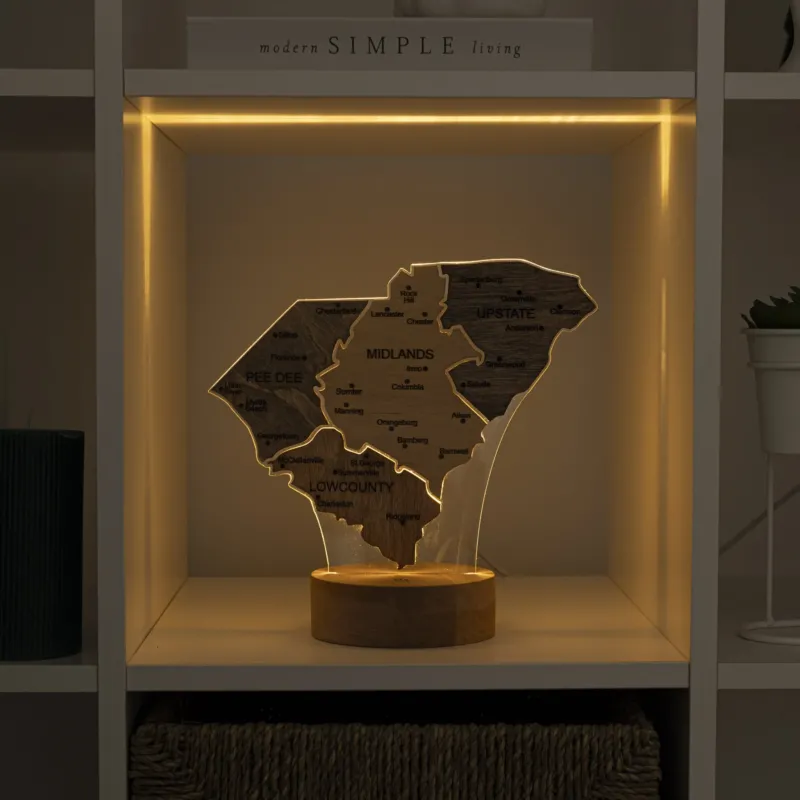 Wooden map of Wisconsin with engraved names, illuminated by a warm light on a shelf.