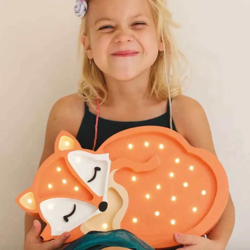 Ein Mädchen mit der Kinder Wand- & Tischleuchte Fuchs in Form eines schlafenden Fuchses lächelt glücklich.