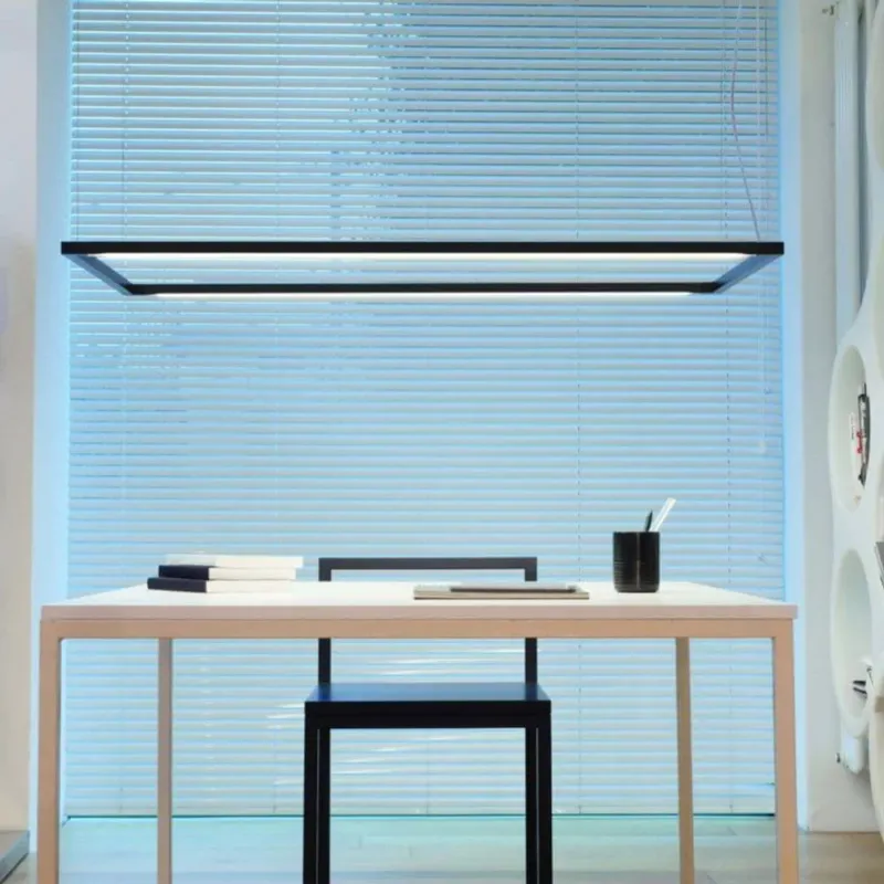 Nemo Spigolo Horizontal LED Hängeleuchte drehbar über einem minimalistischen Schreibtisch mit Holzoberfläche.