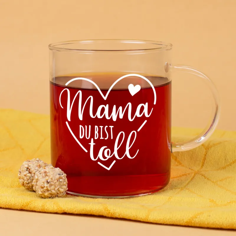 Teeglas mit Aufdruck Mama du bist toll und Herzmotiv auf gelbem Hintergrund mit Gebäck