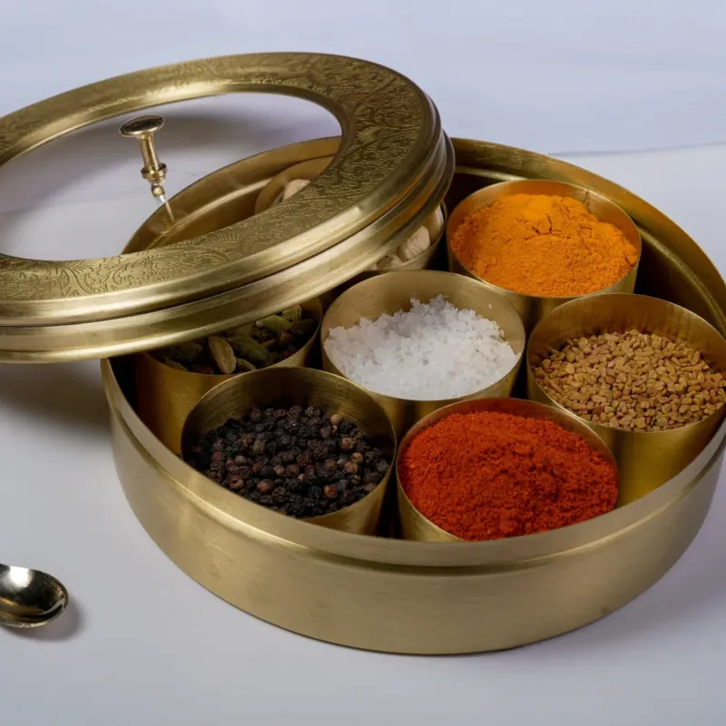 A brass spice box with multiple compartments, each filled with different spices, and a see-through glass lid.