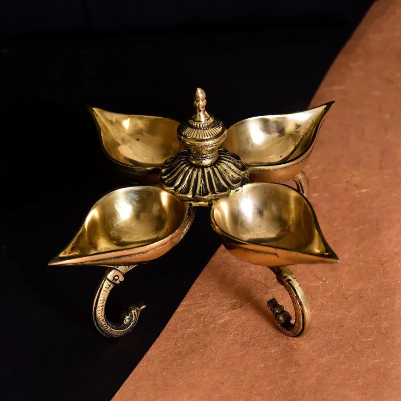 A gold-colored brass oil lamp with four petals, displayed against a contrasting background.