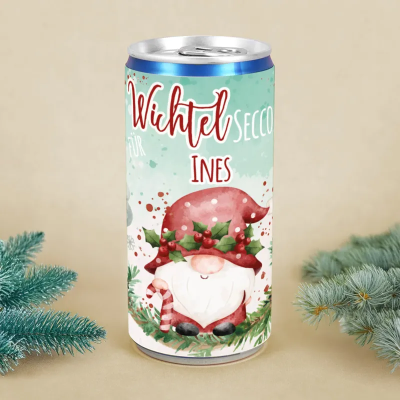 Personalisierte Secco-Dose mit Wichtelmotiv, roter Mütze, Mistelkranz und Name Ines, dekoriert mit Tannenzweigen als Weihnachtsgeschenk.