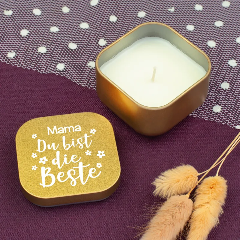 Geöffnete goldene Duftkerze mit Vanilleduft, Deckel mit Aufschrift „Mama Du bist die Beste“ auf violettem Stoff