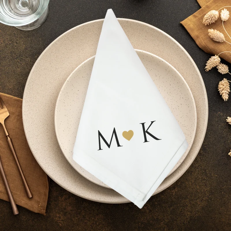 Personalisierte Stoffserviette zur Hochzeit mit Initialen M und K sowie goldenem Herz auf Teller dekoriert