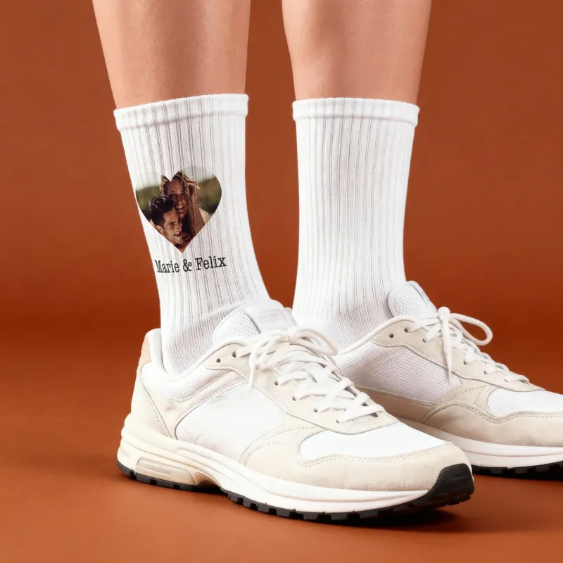 Personalisierte Foto-Socken mit Herzfoto und Wunschtext, getragen am Fuß vor orangem Hintergrund
